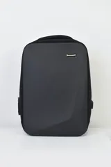 Mochila ejecutiva negra con diseño rígido y geométrico en el frente, asa superior y herraje metálico horizontal. Presenta un puerto USB lateral.