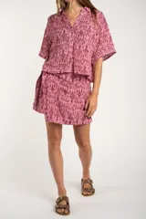 Camisa de manga corta con estampado abstracto en tonos rosa y borgoña. Tiene cuello camisero, cierre frontal con botones y corte oversize.