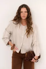 Chaqueta de lino color beige, de manga larga, con cuello redondo y cierre frontal de botones a presión con solapa.