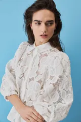 Camisa de broderie color blanco, con cuello clásico, mangas abullonadas y cierre frontal oculto.