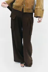 Pantalón cargo de tiro medio en color marrón oscuro, con corte recto y amplio. Presenta bolsillos laterales tipo cargo con solapa y detalle de pliegues frontales. Cierre frontal con cremallera y botón.