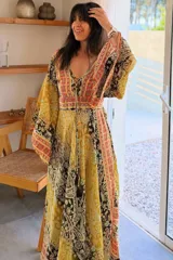 Vestido largo de estilo bohemio, color azul con estampado floral en tonos blancos y detalles geométricos en el escote y la cintura. Posee escote en V con cordones ajustables, mangas amplias tipo kimono y una silueta fluida y holgada.