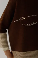 Buzo de lana color beige con bloques de color ocre y bordó en mangas y ruedo. Presenta un bolsillo pequeño en el pecho y costuras decorativas en color bordó.