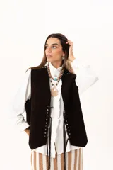 Chaleco oversize confeccionado en cuero descarne, con diseño de terminación en picos. Presenta lazos frontales con ojalillos metálicos y detalle de tachas metálicas en hombros y espalda.