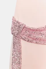 Vestido mini rosado de cuello subido, manga corta amplia y espalda descubierta. Cuenta con detalle de fajín drapeado con aplicación de lentejuelas brillantes y caída lateral.