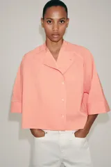 Camisa ZARA Woman Collection confeccionada en hilatura con viscosa, con diseño de rayas finas y color salmón. Presenta cuello perkins, mangas por debajo del codo, bajo asimétrico y cierre frontal cruzado con botones.