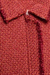 Chaqueta corta de tweed en color rojo, con cuello solapa, manga larga y bolsillos frontales con solapa. Presenta detalles deshilachados en los bordes y cierre frontal con cremallera oculta.