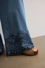 Pantalón de jean de corte holgado y pernera ancha, con cintura elástica y detalle de bordado oscuro con diseño floral y perforaciones en el bajo.