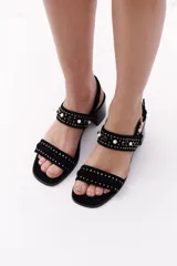 Sandalias de cuero color marrón con dos tiras horizontales, una sobre los dedos y otra sobre el empeine, ambas decoradas con tachas. Tienen taco cuadrado de madera y cierre con hebilla.