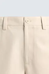 Pantalón chino de algodón color beige, de corte relajado (relaxed fit) y tiro medio. Presenta bolsillos delanteros y bolsillos traseros de vivo con cierre de cremallera y botón.