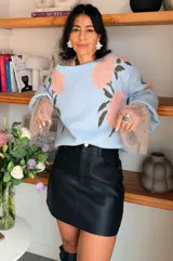 Suéter de punto color celeste con estampado floral en tonos rosados y verdes. Presenta mangas amplias con puños de encaje en color nude y cuello redondo.