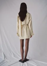Chaqueta de algodón elastizado color beige, con cuello alto, cierre frontal de botonadura simple, mangas largas y cinturón ajustable del mismo tejido.