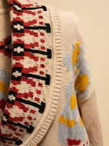 Cardigan de tejido grueso con cuello shawl, estampado tribal en tonos rojo arcilla, crema y negro, con cierre frontal de botones y puños en tono kontrastante.