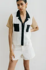 Camisa de manga corta con diseño color block, combinando paneles blancos, verde oliva y detalles en negro (cuello, tapeta de botones y bolsillos de parche).
