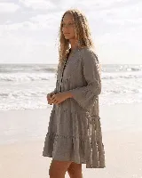 Vestido corto de lino natural color gris, con diseño amplio de capas, escote en V con botones frontales y mangas largas con volados en los puños.