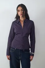 Camisa de manga larga confeccionada en popelina de algodón, con diseño de rayas verticales finas en tonos azul oscuro y naranja. Presenta cuello clásico, cierre frontal con cremallera y un corte ajustado al cuerpo.