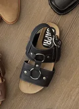 Sandalia plana negra de cuero vacuno, estilo pescador o gladiador, con tiras anchas ajustables con hebillas metálicas y remaches. Presenta costuras blancas contrastantes y plantilla anatómica.