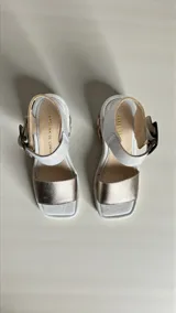 Sandalias de cuero color blanco y dorado, con taco ancho intervenido con arte pintado a mano, tira frontal metalizada, tira al tobillo con hebilla metálica y plataforma baja.