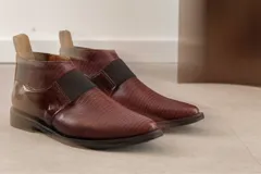 Zapato tipo botineta de cuero color bordó con textura grabada, diseño de punta fina y detalles de elásticos laterales en color negro.