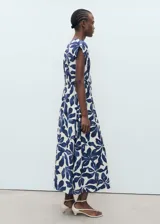 Vestido largo de corte evasé con estampado botánico en azul sobre fondo crudo. Presenta cuello de pico, mangas cortas y un panel fruncido en la cintura con cordón ajustable.