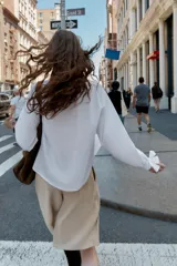 Camisa blanca de manga larga con cuello solapa y cierre frontal de botones. Los puños terminan con lazos anudados en el mismo tejido.