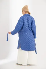 Campera azul capitoneada de nylon con forro de algodón y relleno de poliéster. Tiene ruedo curvo, largo midi, cinta para atar a la cintura y bolsillos delanteros.