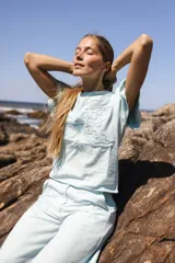 Blusa de lino color celeste, con bordado en relieve de formas orgánicas en el frente y terminaciones desflecadas. Tiene silueta recta y mangas cortas.