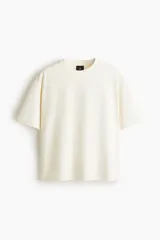 Remera de algodón en punto liviano color beige, con diseño boxy de hombros caídos, cuello redondo con ribete acanalado y corte oversized.