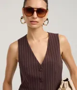 Chaleco entallado de mujer, color marrón oscuro con finas rayas verticales blancas (rayas de giz). Presenta escote en V, cierre frontal con botones forrados y bolsillos falsos.