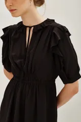 Vestido corto negro con mangas cortas con volados, escote con cuello redondo y abertura con lazos. Presenta cintura ajustada con frunces y falda corta con caída.