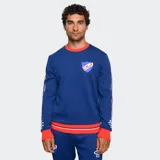 Buzo de cuello redondo color azul, con detalles en rojo y blanco en cuello, puños y ruedo. Presenta el escudo del Club Nacional de Football en el pecho y bandas laterales con diseño deportivo en las mangas.