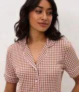 Pijama largo de dos piezas confeccionado en ribana con estampado de cuadros vichy en tonos marrón y blanco. Incluye una blusa de manga corta con cuello solapa, cierre frontal de botones y detalles de vivo contrastante, y un pantalón de pierna recta con cintura elástica.