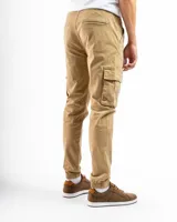 Pantalón cargo estilo jogger color verde oliva, confeccionado en algodón con spandex. Presenta cintura con elástico y pasadores para cinturón, cierre frontal y puños ajustados en los tobillos. Cuenta con múltiples bolsillos cargo laterales.