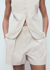 Short de tiro alto en color beige, con diseño recto, detalle de pinzas delanteras y bolsillos laterales. Cuenta con cierre oculto de botón, gancho y cremallera.