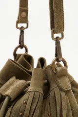 Cartera tipo bucket bag de cuero vacuno color verde oliva, con diseño de flecos largos y detalles de tachas metálicas. Cuenta con cierre de cordón ajustable y correa larga para llevar al hombro o cruzada.
