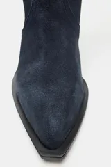 Bota alta de estilo cowboy confeccionada en serraje de color azul marino, con tacón medio en bloque y puntera perfilada. Presenta costuras decorativas en el cuerpo y diseño de calce fácil.