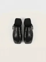 Zueco de cuero encerado color negro, con diseño de punta cuadrada, detalle de tachas metálicas en el lateral y hebilla ajustable en la capellada. Cuenta con suela de goma.