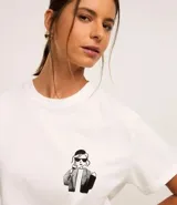 Blusa blanca de algodón con cuello redondo y mangas cortas. Presenta un estampado de una caricatura de una mujer con boina, lentes de sol y un trago en la mano.