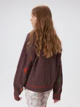 Sweater de punto con diseño de ochos en color verde, cuello redondo con detalle de franja en contraste, y apliques de rombos en las mangas. Presenta un bordado con la letra M en el pecho.