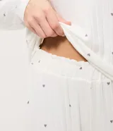 Pijama de dos piezas confeccionado en tejido de punto acanalado color blanco con estampado de pequeñas cerezas. Incluye una blusa de cuello redondo y manga larga, y un pantalón con cintura elástica y puños ajustados en los tobillos.