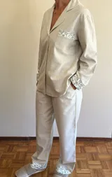 Pijama de viyela de algodón color beige con rayas verticales finas. El conjunto incluye una camisa de manga larga abotonada con detalles de estampado floral en puños y bolsillo, y un pantalón a juego con el mismo estampado floral en los bajos.