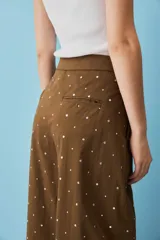 Pantalón marrón de corte ancho, tiro alto y diseño holgado, adornado con pequeños apliques metálicos distribuidos por toda la prenda.