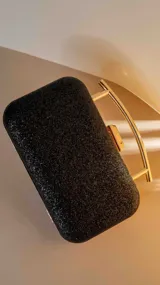 Clutch rígido rectangular color negro con glitter y herrajes dorados. Asa metálica dorada en forma de arco. Cierre con broche a presión.