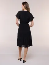 Vestido midi blanco de calce suelto y caída fluida, con escote en V, cuello a la base y apertura abotonada con detalle de puntilla. Cuenta con cintura elastizada con lazo para anudar a tono, mangas cortas con volados y falda con volantes escalonados.