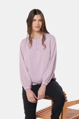 Blusa de manga larga con cuello redondo y cierre frontal parcial mediante botones forrados. Presenta diseño de doble capa en el frente y puños abotonados.