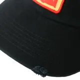 Gorra de béisbol negra con visera curva y parche bordado en el frente con diseño abstracto en amarillo y rojo. Presenta detalles desgastados y roturas en la visera y el frente.
