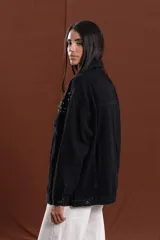 Campera de jean negra con tachas metálicas en los hombros y parte superior de la espalda. Tiene cuello camisero, botones frontales y bolsillos en el pecho.