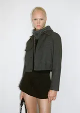 Chaqueta corta de tweed a cuadros grises, con cuello camisero, solapas decorativas, cierre frontal con botones y bajo con goma elástica.