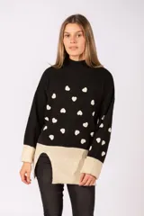 Sweater de punto negro con estampado de corazones blancos, cuello alto y puños en color beige. Presenta un diseño con tajos laterales y ruedo en contraste de color beige.