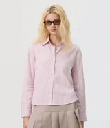 Camisa oversized de popelina de algodón, con diseño a rayas en tonos rosados y azules, cuello clásico, mangas largas con puños abotonados y cierre frontal de botones.